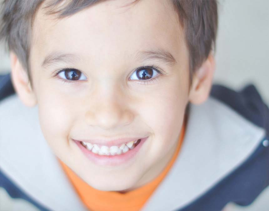 Niño sonriendo, vestido con una playera naranja y chamarra blanco con azul. Su cabello es castaño y corto