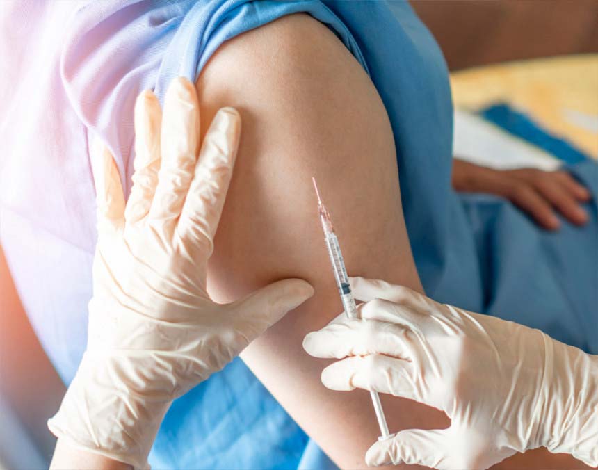 Médico con guantes blancos sosteniendo una jeringa para vacunar a un paciente en el brazo derecho