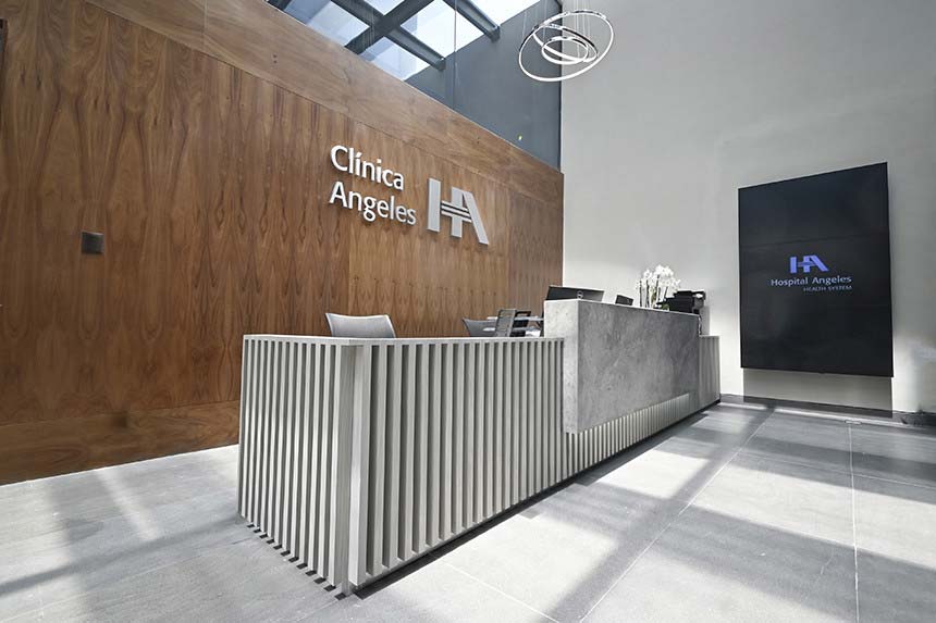 Recepción de Clínica Angeles. Con mostrador gris, pared café atrás con logo de Clínica Angeles en letras grandes grises
