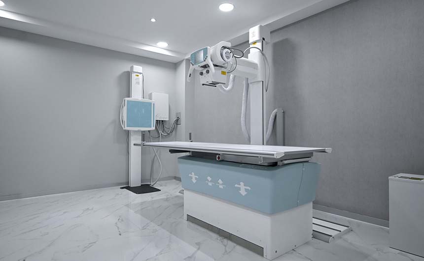 Equipo de rayos X en color blanco con azul, dentro de un cuarto con paredes grises de la Clínica Angeles