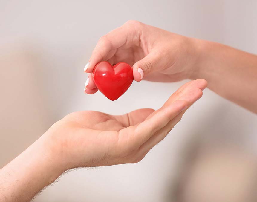 Mano de una mujer a punto de colocar un corazón de color rojo en la mano de un paciente