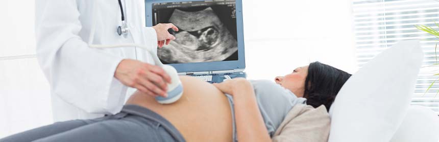 Mujer embarazada recostada en la camilla de un consultorio, mientras el médico le realiza un ultrasonido y ven al bebé en el monitor