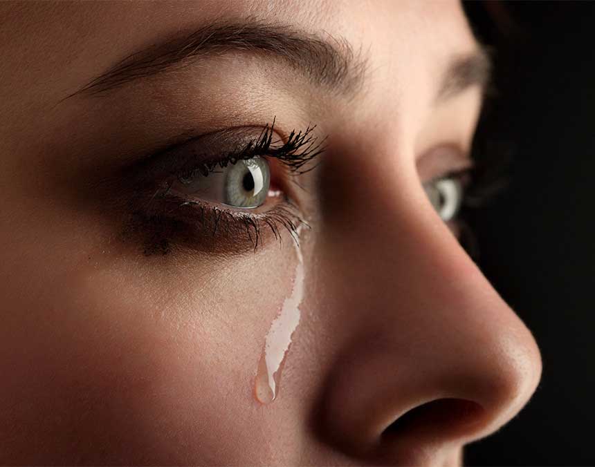 Rostro de una mujer de ojos verdes con una lágrima en su mejilla derecha