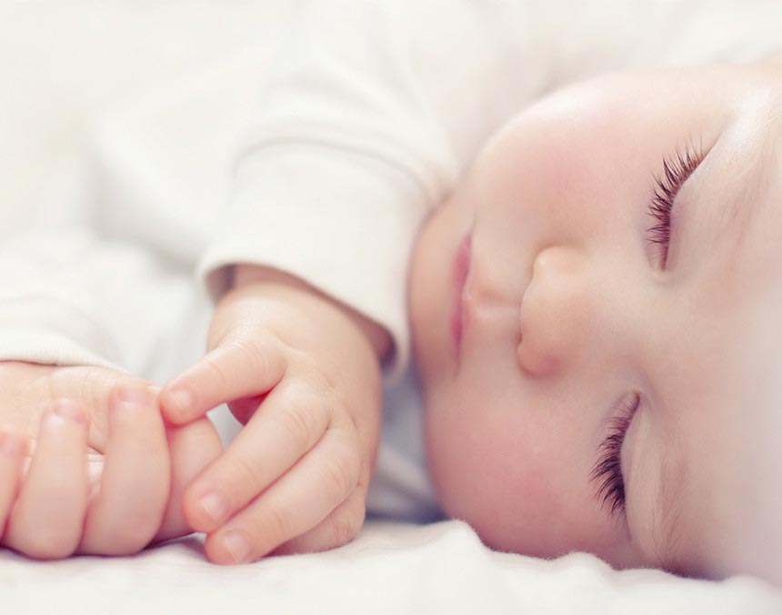 Bebé recién nacido acostado sobre una cama y dormido. Viste un body de color blanco