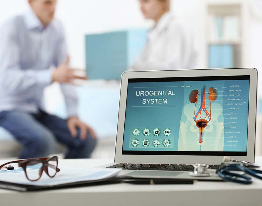 Laptop gris mostrando la imagen gráfica del sistema urinario. Al fondo está el paciente sentado y una doctora parada a su lado