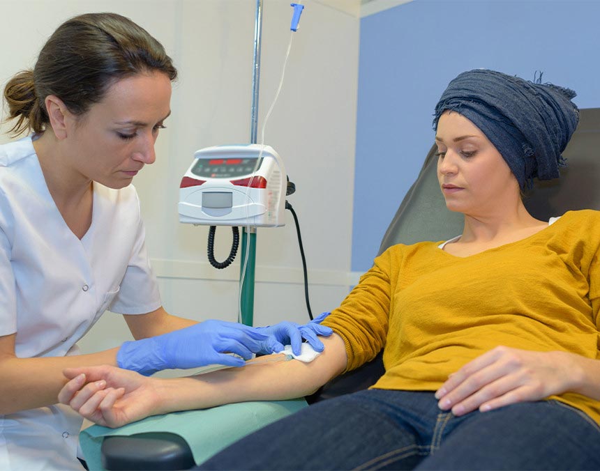 Paciente oncológico sentada para recibir su tratamiento de quimioterapia, mientras una enfermera le coloca el suero intravenoso