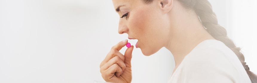 Mujer joven agarrando una pastilla de color rosa y está a punto de tomársela