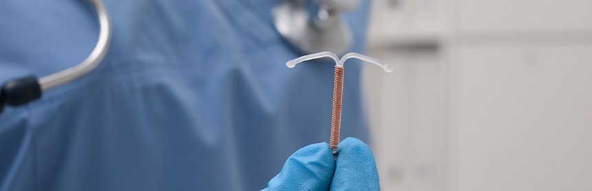 Mano de un médico con un guante azul, sosteniendo un dispositivo intrauterino de cobre