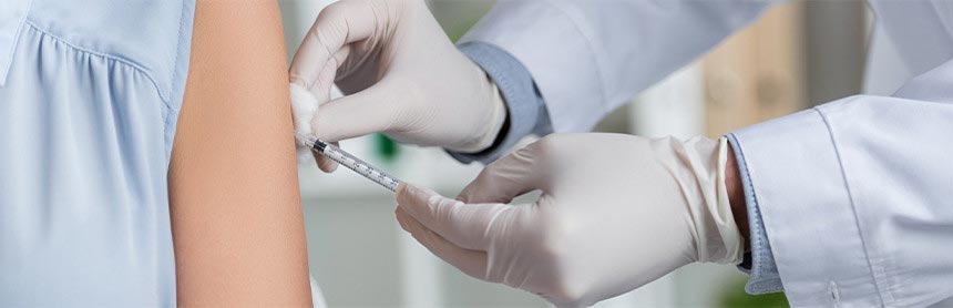 Doctor con bata y guantes blancos, vacunando a una paciente en el brazo izquierdo