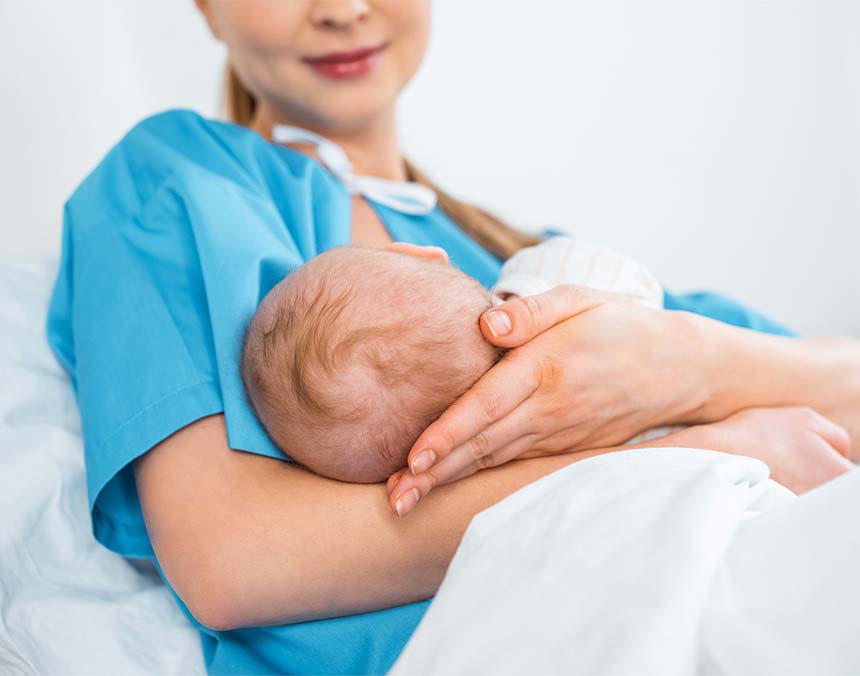 Mujer que acaba de dar a luz vestida con una bata azul, cargando a su bebé recién nacido