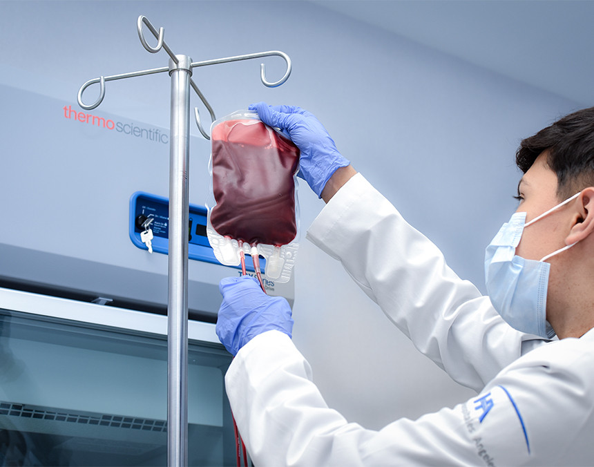 Médico de Hospital Angeles con bata blanca y guantes azules, colocando la bolsa de transfusión sanguínea en el porta sueros