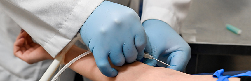Médico con bata blanca y guantes azules, sacando sangre del brazo derecho de un paciente