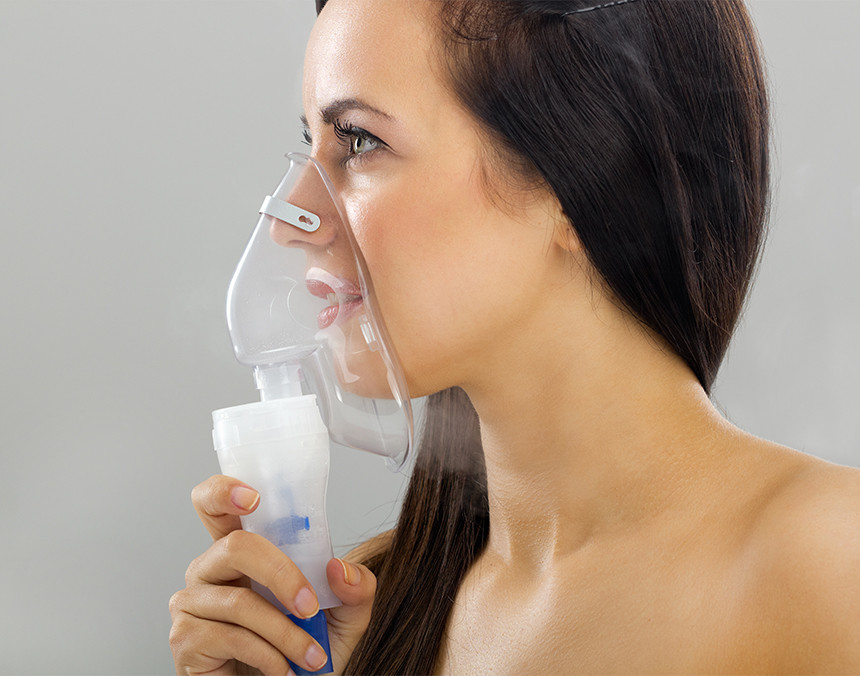 Mujer joven sosteniendo un nebulizador de oxígeno con su mano derecha y colocándoselo en la nariz