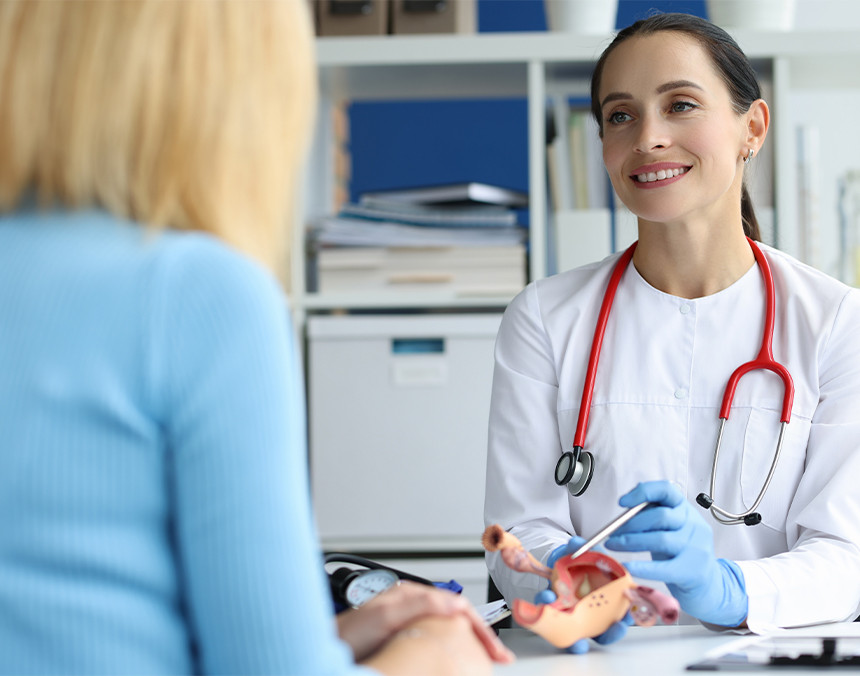 Doctora con bata blanca mostrándole un prototipo de un útero a una paciente en un consultorio médico