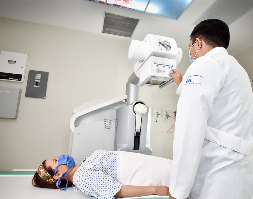Paciente acostada sobre la camilla de un equipo de rayos X, mientras un médico de Hospital Angeles está a su lado