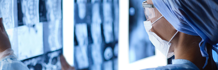 Doctora con pijama para cirugía y gorro azul, y cubrebocas; observando detenidamente unas radiografías