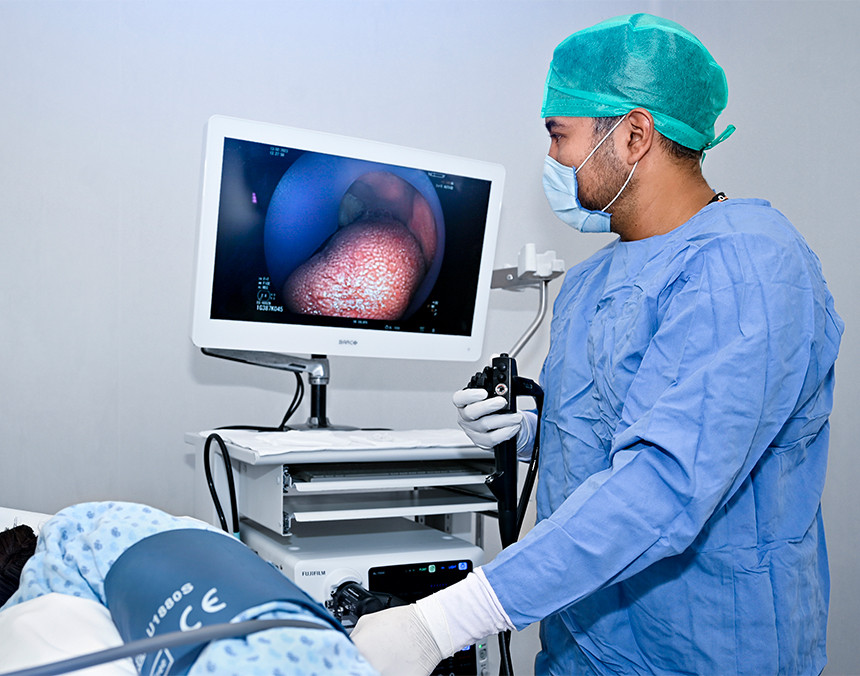 Médico con pijama azul para cirugía realizando un estudio de endoscopia digestiva a una paciente que se encuentra recostada