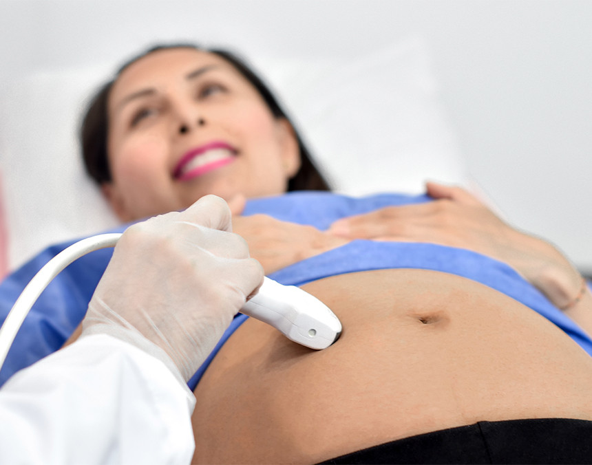 Mano de un médico con guante blanco realizando un ultrasonido a una paciente que está embarazada