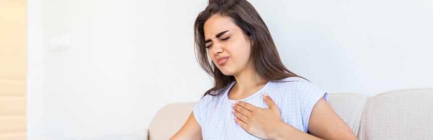 Mujer joven vestida con playera blanca sintiendo dolor en el pecho como síntoma de una arritmia cardiaca