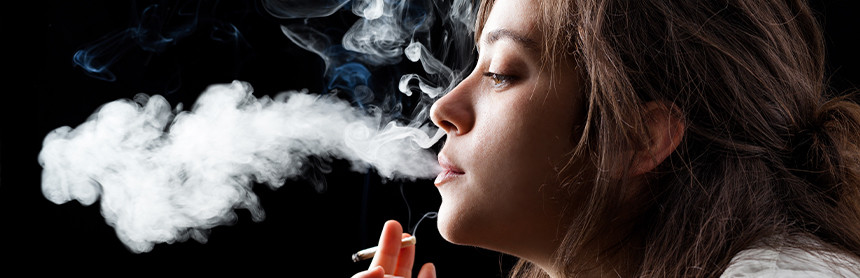 Mujer joven sosteniendo un cigarro y soltando el humo por la boca