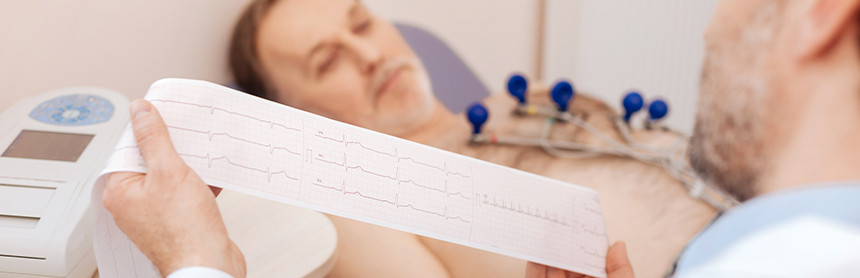 Médico analizando los resultados del electrocardiograma mientras el paciente está acostado en una mesa de exploración