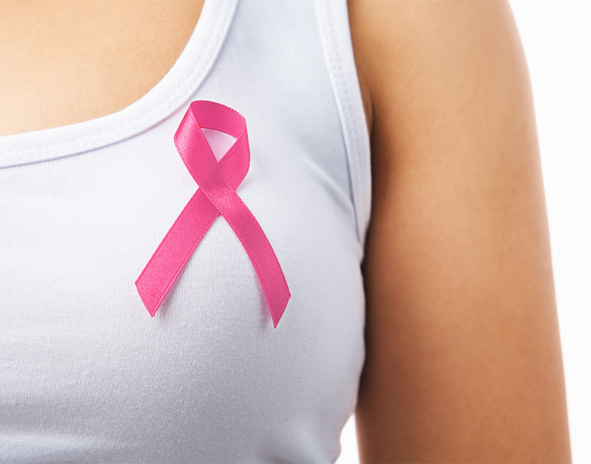 Primer plano de una mujer vestida con una camiseta blanca con un lazo rosa en su pecho representando la lucha contra el cáncer de mama