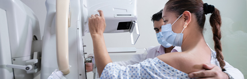 Paciente realizándose una mastografía en Hospital Angeles Tampico. Usa una bata para paciente blanca. Un doctor está a su lado