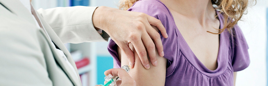 Médico con bata blanca vacunando a una paciente contra el virus del papiloma humano en el brazo derecho
