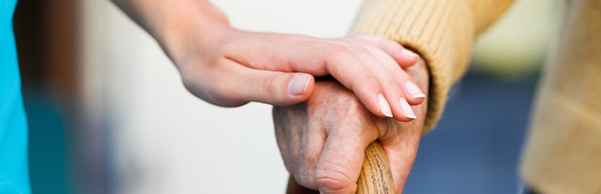 Mano de una persona joven colocada sobre la mano de un adulto mayor