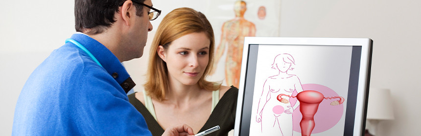Mujer joven en consulta ginecológica. El médico le muestra en una computadora el diagrama de un útero