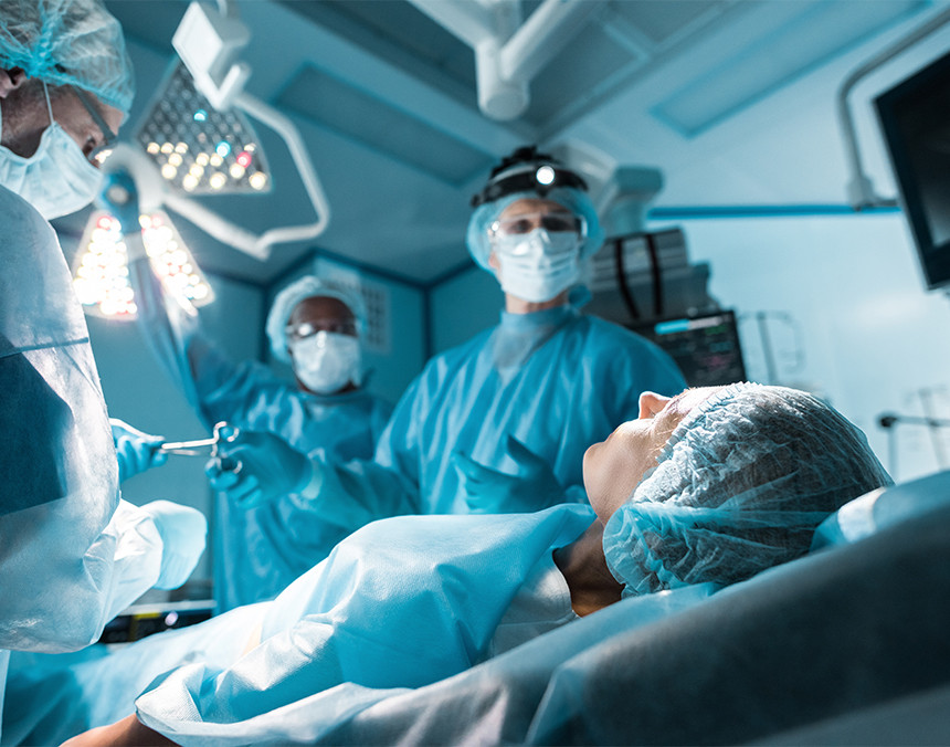 Paciente sedada y acostada en una camilla quirúrgica. Hay tres médicos con pijamas azules para cirugía a su alrededor