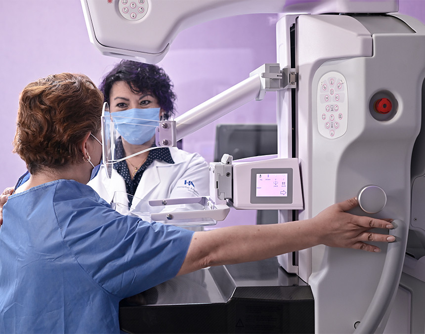 Paciente con pijama azul a punto de realizarse una mastografía. Una doctora con bata blanca está a su lado