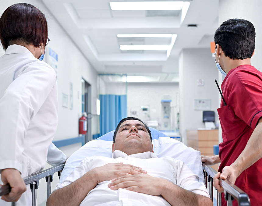 Doctora con bata blanca y enfermero con uniforme rojo, llevando a un paciente al área de urgencias en una camilla
