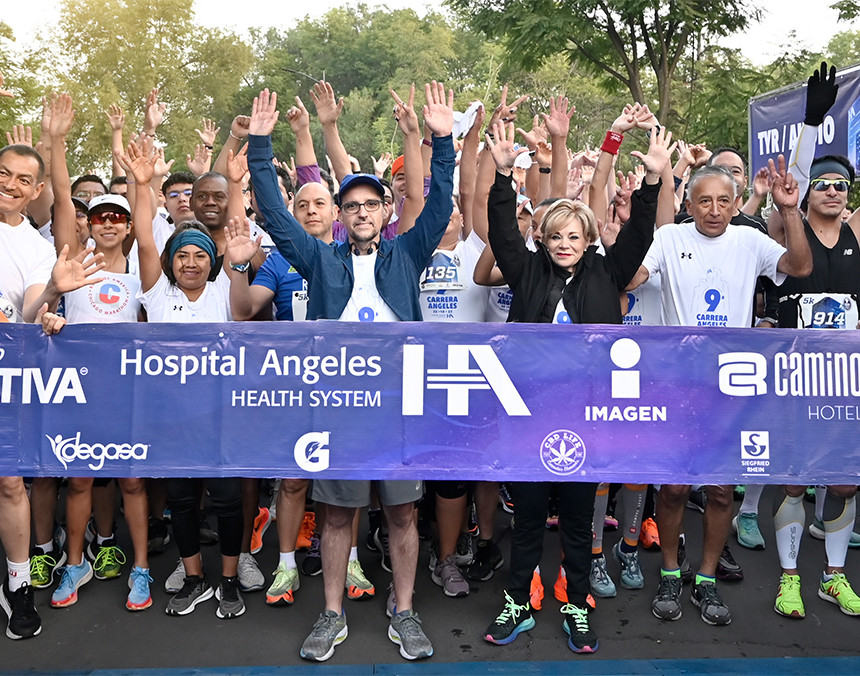 Varias personas listas para correr, levantando las manos. Están detrás de una cinta morada con el logo de Hospital Angeles