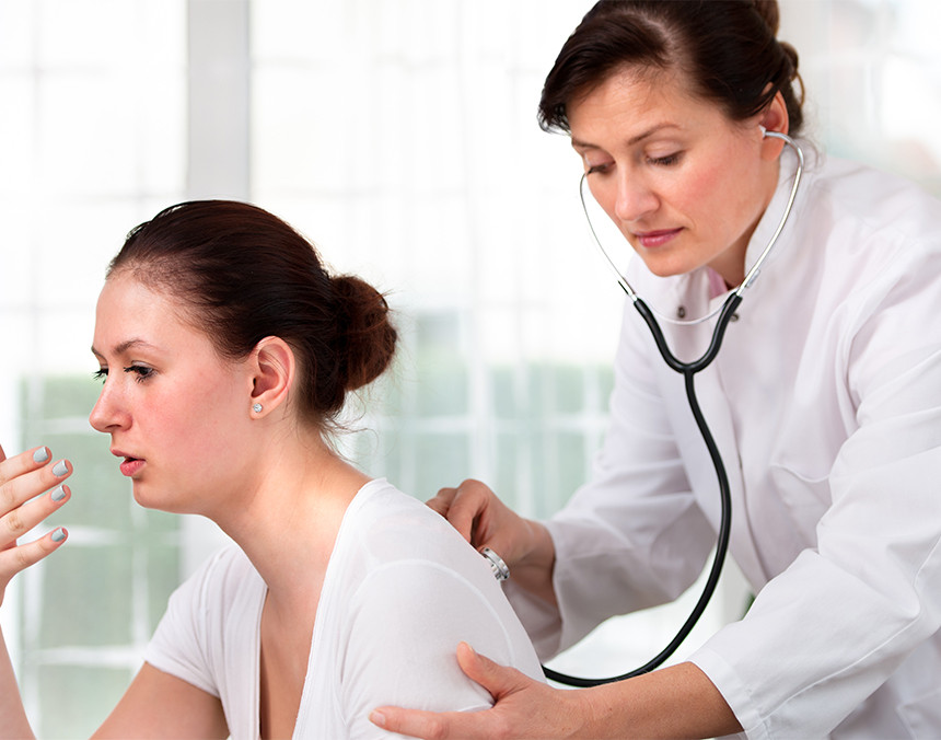 Doctora con bata blanca escuchando los pulmones de una paciente con un estetoscopio