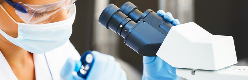 Doctora con uniforme blanco y guantes azules analizando una muestra de laboratorio en un microscopio