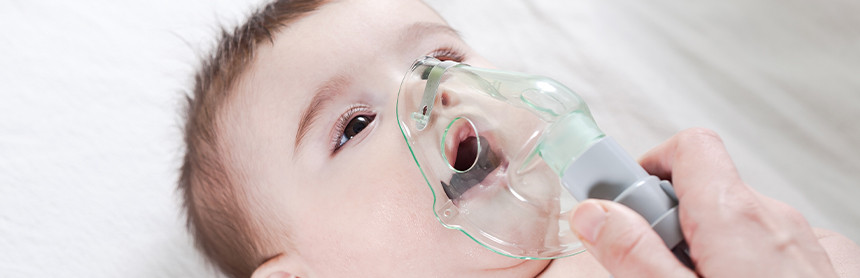 Bebé con cabello castaño acostado y recibiendo soporte respiratorio con un inhalador