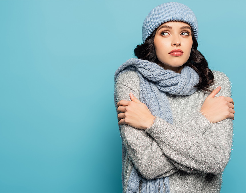 Mujer joven con frío vestida con ropa invernal, gorro y bufanda azules y suéter gris