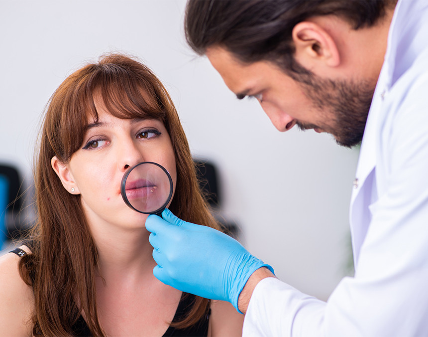 Dermatólogo con bata blanca y guantes, evaluando el sarpullido en la boca de una paciente con herpes