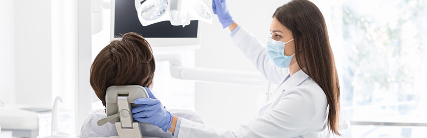 Dentista con bata blanca, guantes y cubrebocas azules realizando una exploración dental a un paciente