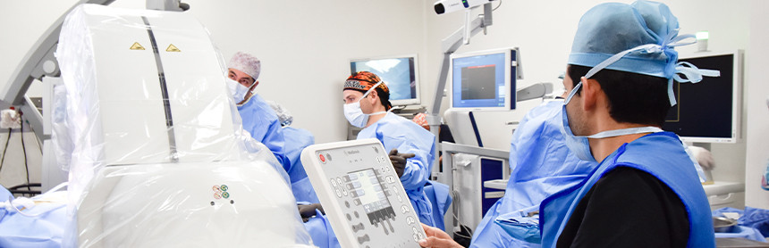 Tres médicos con pijamas azules realizando una cirugía de columna con el sistema O-ARM dentro de un quirófano