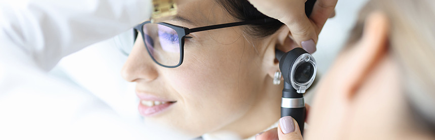 Doctora realizando un examen del oído a una paciente que usa lentes
