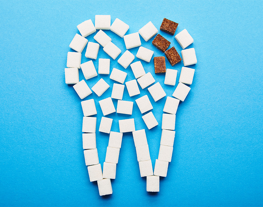Vista superior de varios cubos de azúcar acomodados en forma de diente. Hay unos cubos de azúcar morena denotando caries