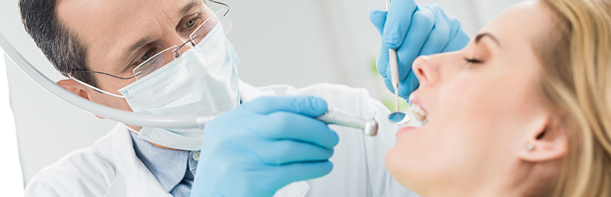 Dentista con cubrebocas y guantes azules realizando un examen bucal a una paciente