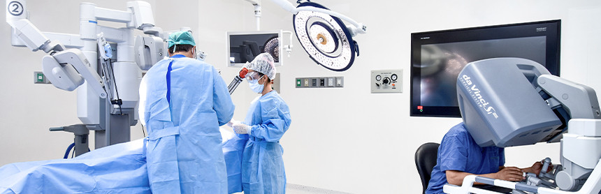 Tres médicos con pijamas azules y cubrebocas realizando un procedimiento quirúrgico con el Sistema Quirúrgico Robótico Da Vinci en un quirófano