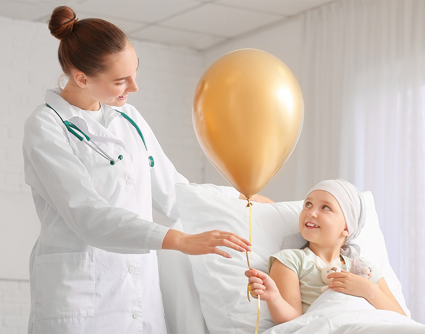 Doctora sonriendo entregándole un globo dorado a una niña con cáncer
