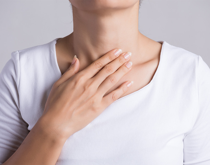 Primer plano de una mujer vestida con una blusa blanca colocando su mano derecha en la zona de la garganta