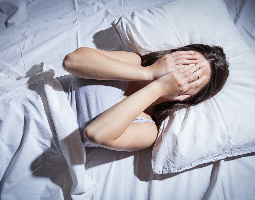 Mujer joven con insomnio acostada en una cama cubriendo su cara con ambas manos