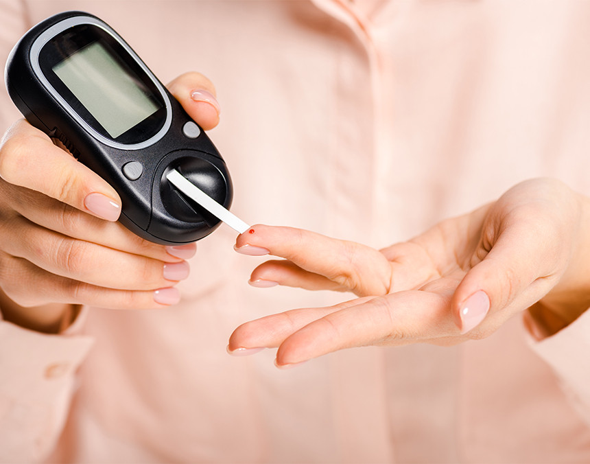 Primer plano de las manos de una mujer de la tercera edad midiendo sus niveles de glucosa con un glucómetro negro