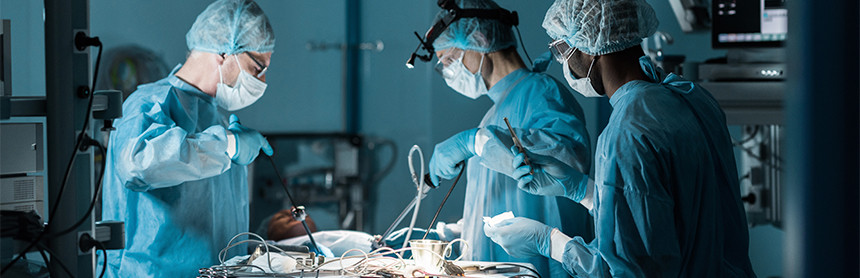 Tres médicos vestidos con pijamas azules para cirugía, cubrebocas y gorros realizando un procedimiento quirúrgico